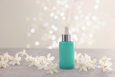 Photo of Cosmetic product in bottle and beautiful jasmine flowers on grey table against beige background with blurred lights