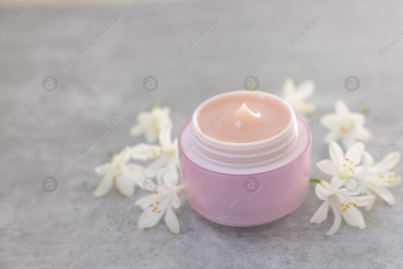 Photo of Cream in jar and beautiful jasmine flowers on grey table, closeup. Space for text