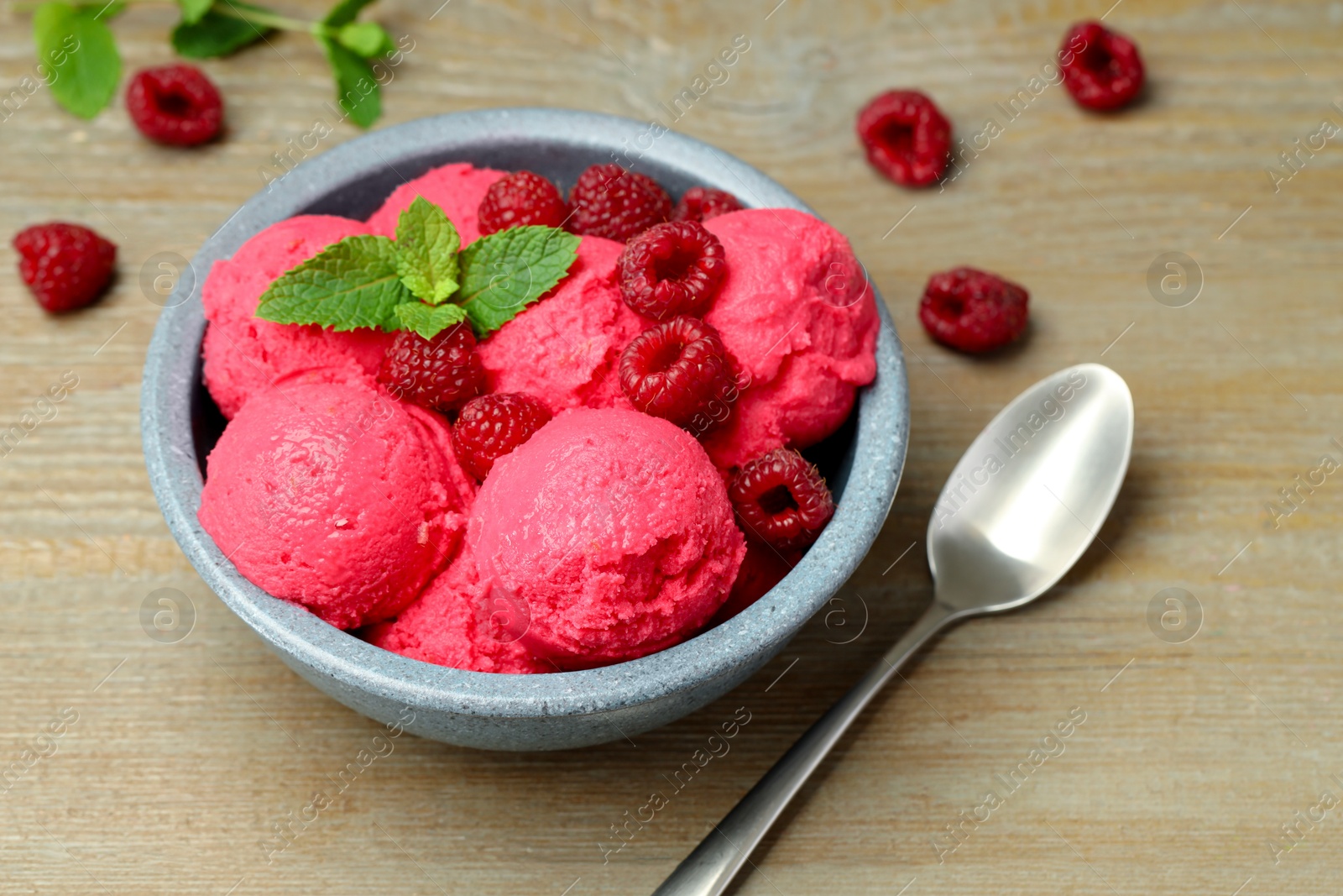 Photo of Delicious raspberry sorbet with fresh berries in bowl and spoon on wooden table