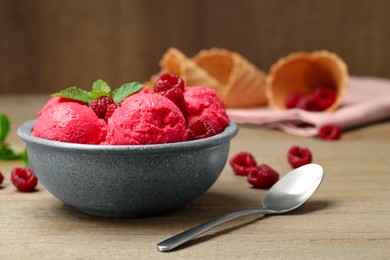 Photo of Delicious raspberry sorbet with fresh berries in bowl and spoon on wooden table