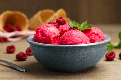 Photo of Delicious raspberry sorbet, fresh berries and mint in bowl on wooden table, closeup