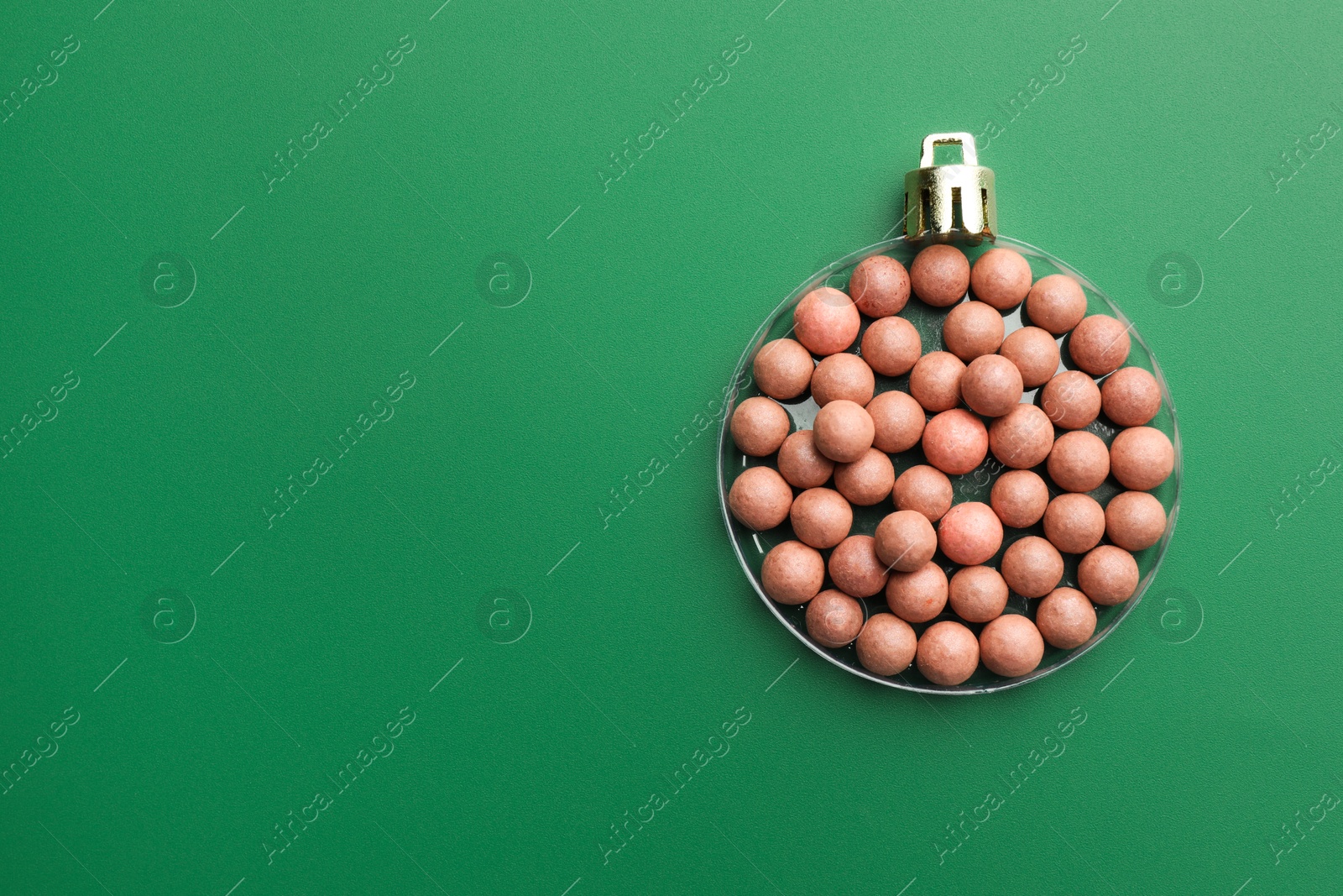 Photo of Christmas ball made of cosmetic product on green background, top view. Space for text