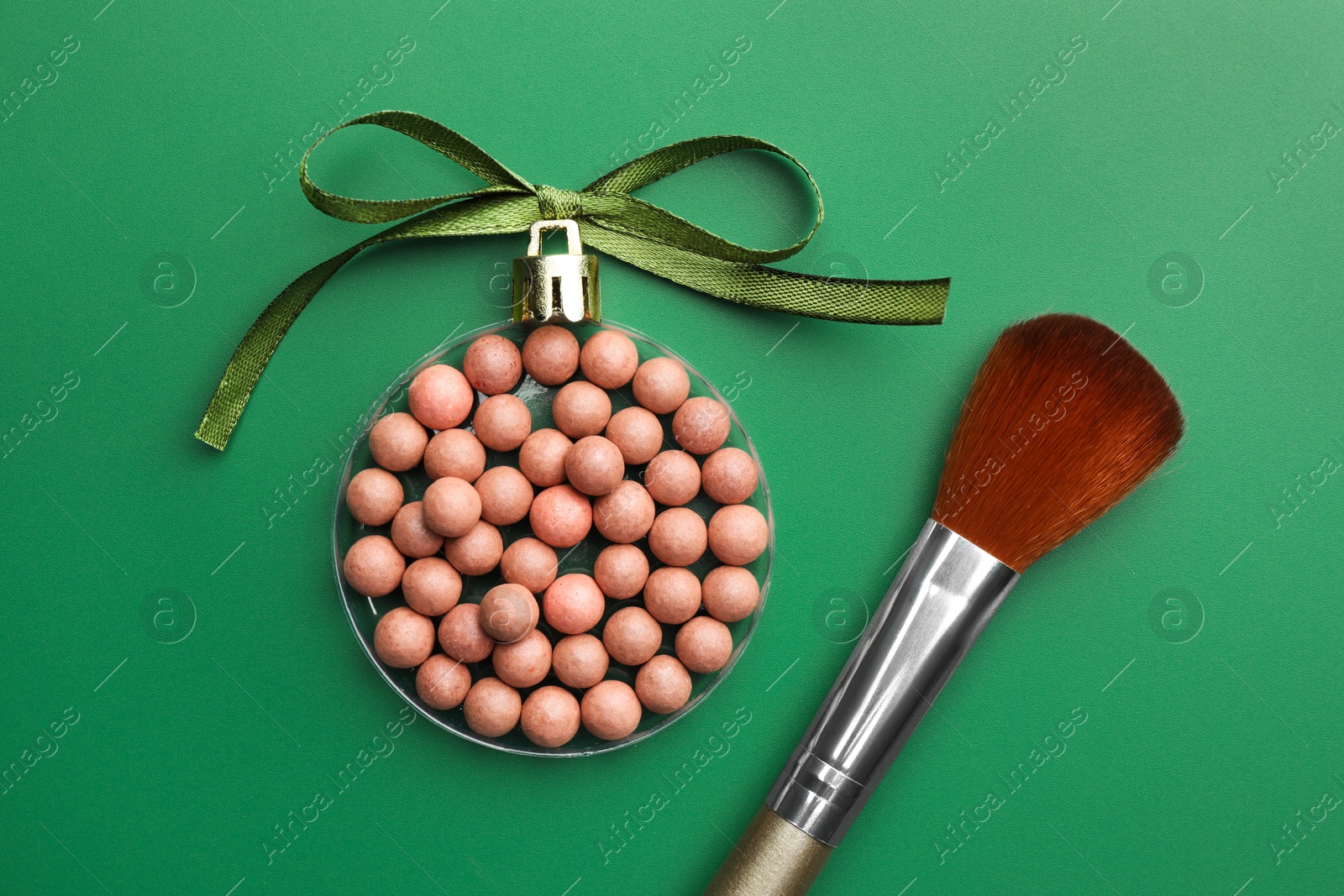 Photo of Christmas ball made of cosmetic product, bow and makeup brush on green background, flat lay