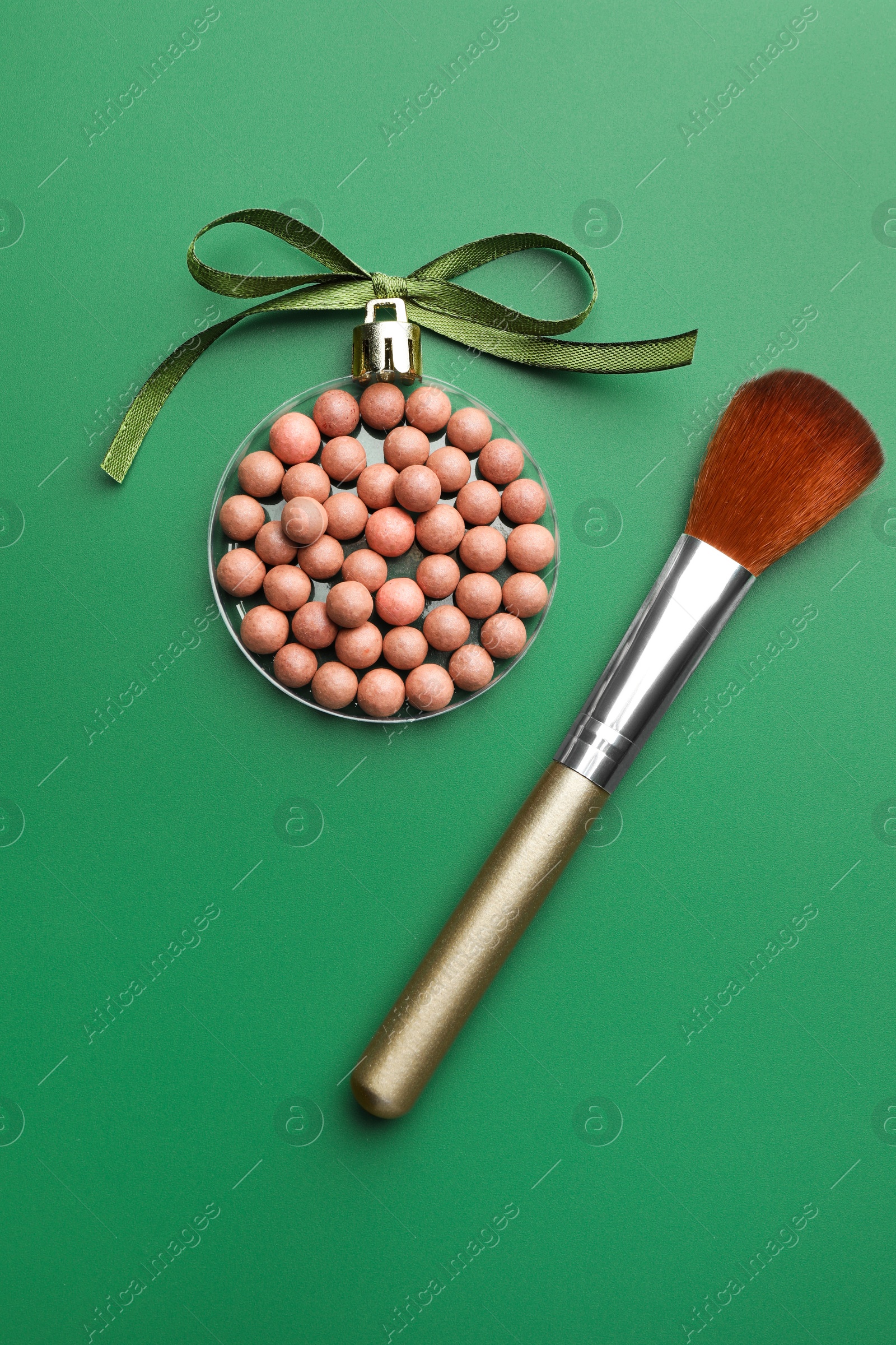 Photo of Christmas ball made of cosmetic product, bow and makeup brush on green background, flat lay