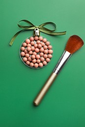 Photo of Christmas ball made of cosmetic product, bow and makeup brush on green background, flat lay