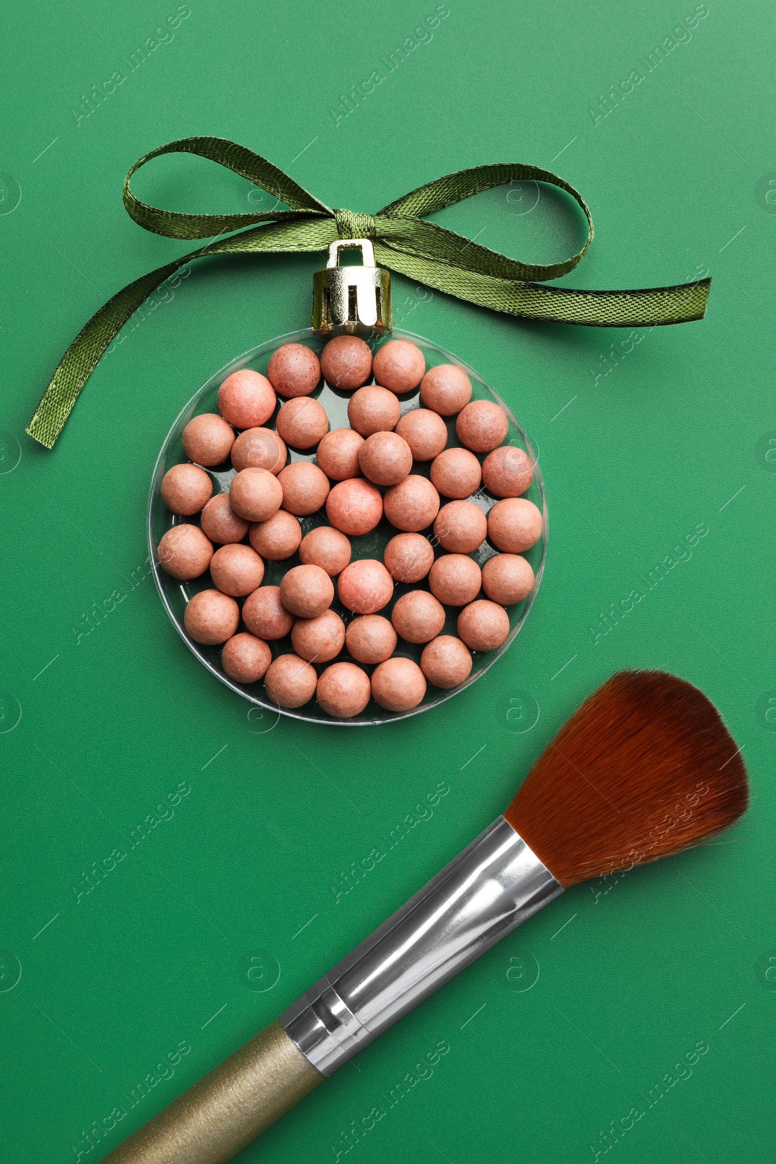 Photo of Christmas ball made of cosmetic product, bow and makeup brush on green background, flat lay