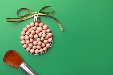 Photo of Christmas ball made of cosmetic product, bow and makeup brush on green background, flat lay. Space for text