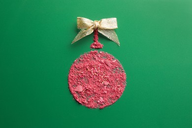 Christmas ball made of blush and bow on green background, top view