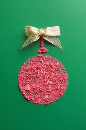 Christmas ball made of blush and bow on green background, top view