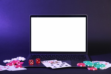 Photo of Online poker. Playing cards, chips, dice and laptop on dark table