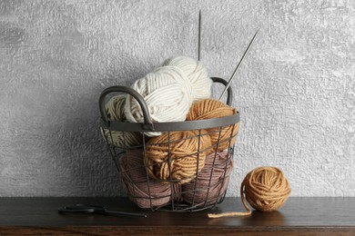 Photo of Basket with colorful yarns, knitting needles and scissors on wooden shelf indoors