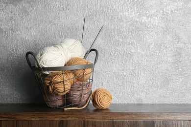 Basket with colorful yarns and knitting needles on wooden shelf indoors. Space for text