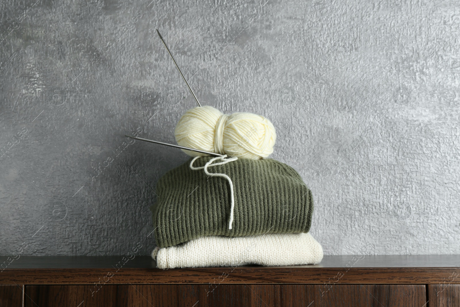 Photo of Skein of yarn, knitting needles and sweaters on wooden shelf indoors