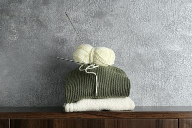 Photo of Skein of yarn, knitting needles and sweaters on wooden shelf indoors