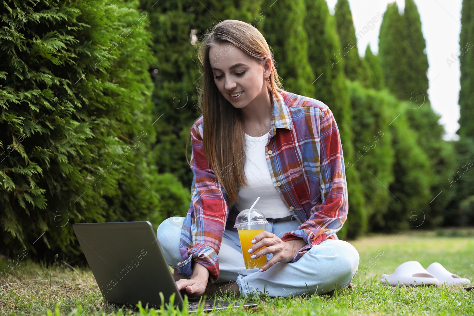 Photo of Woman with juice using laptop on green lawn in park