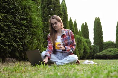 Photo of Woman with juice using laptop on green lawn in park