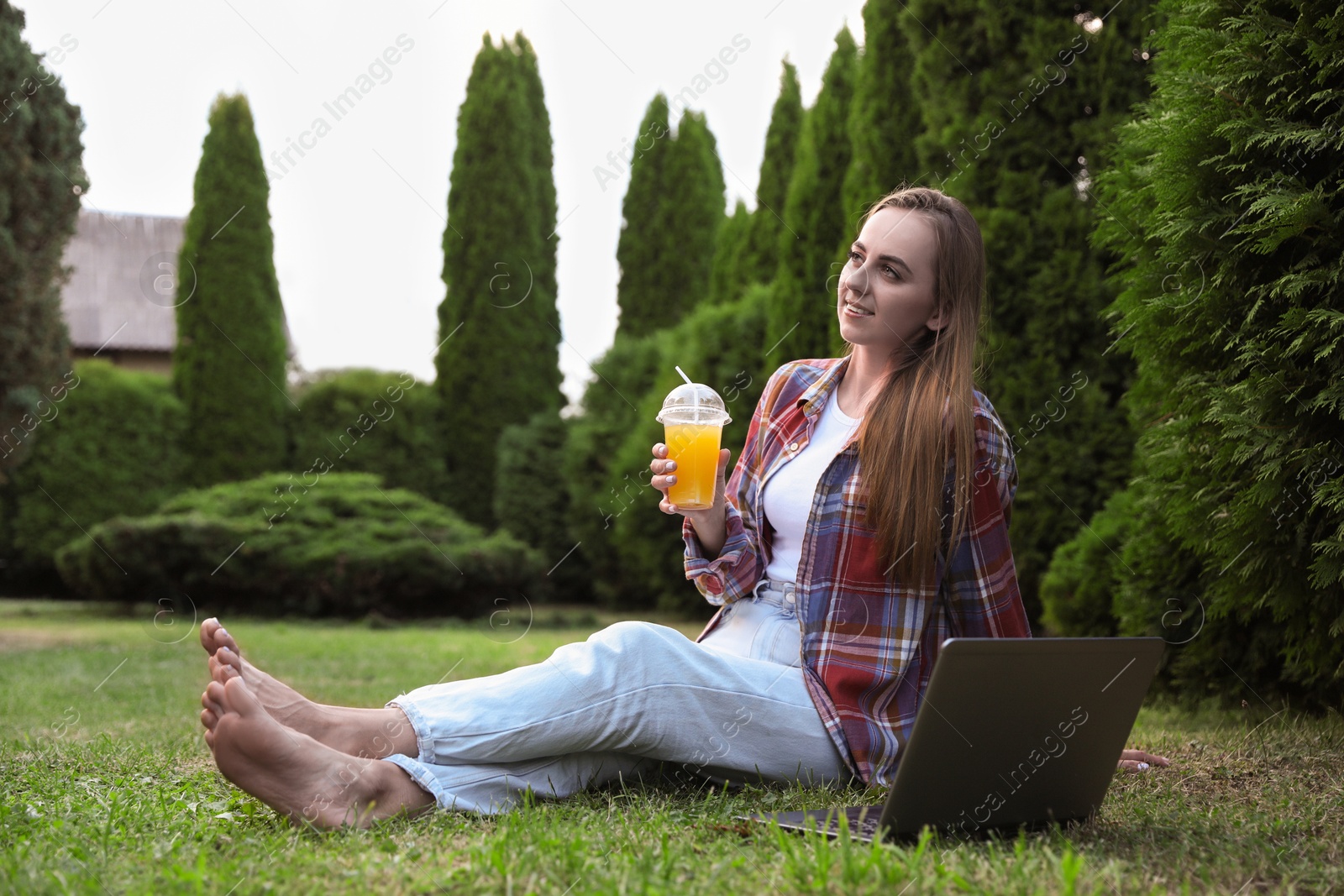 Photo of Woman with juice sitting near laptop on green lawn in park