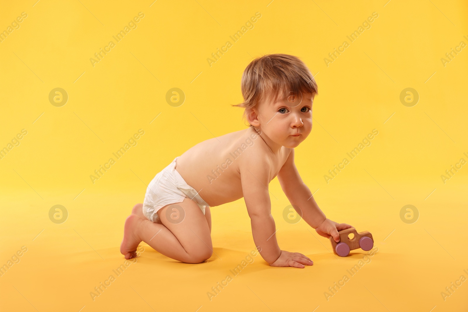 Photo of Little child in diaper with toy on orange background