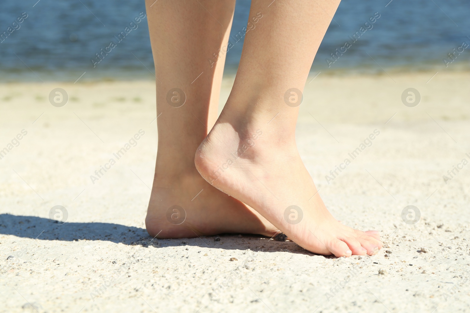 Photo of Woman walking barefoot on sand outdoors, closeup