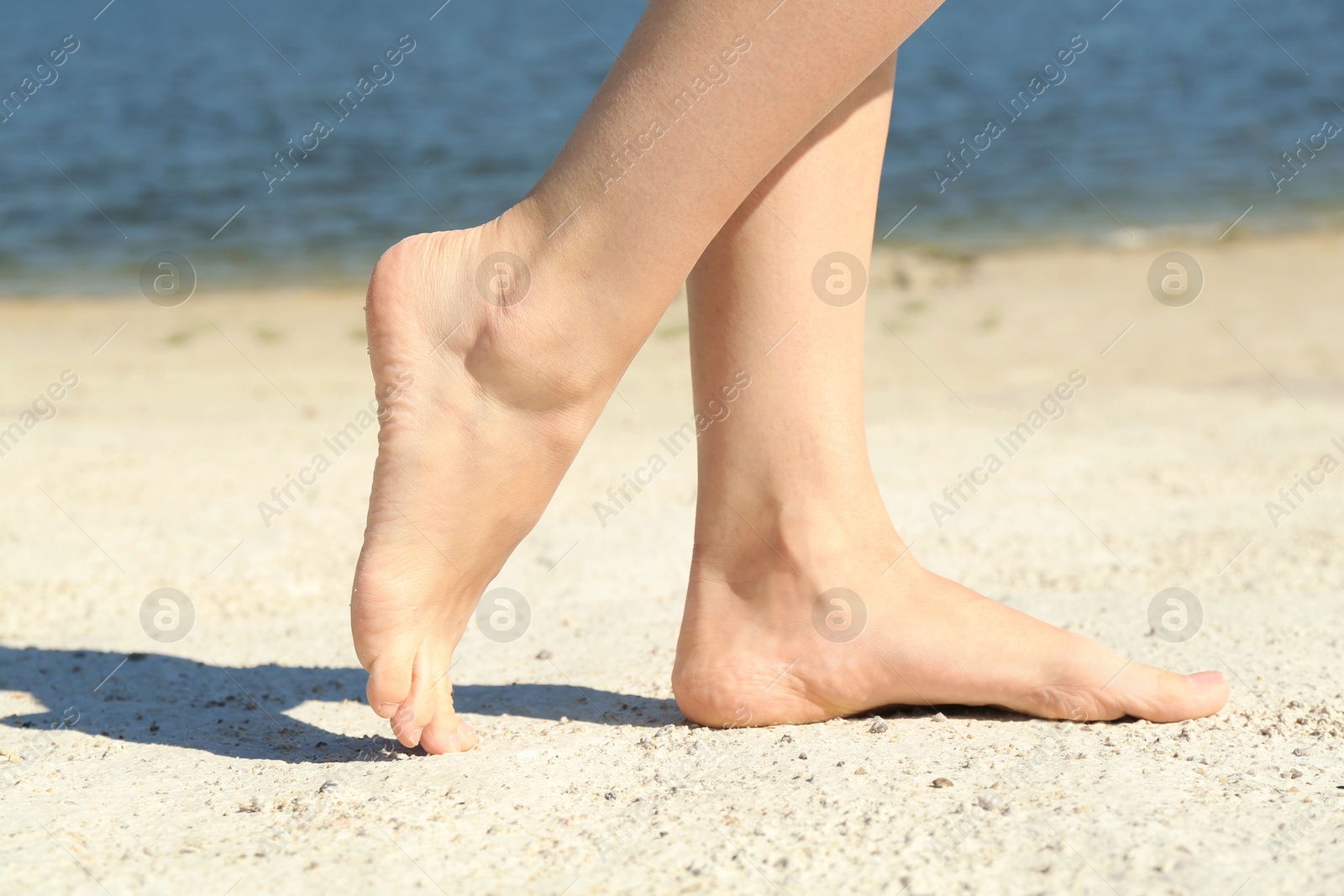 Photo of Woman walking barefoot on sand outdoors, closeup