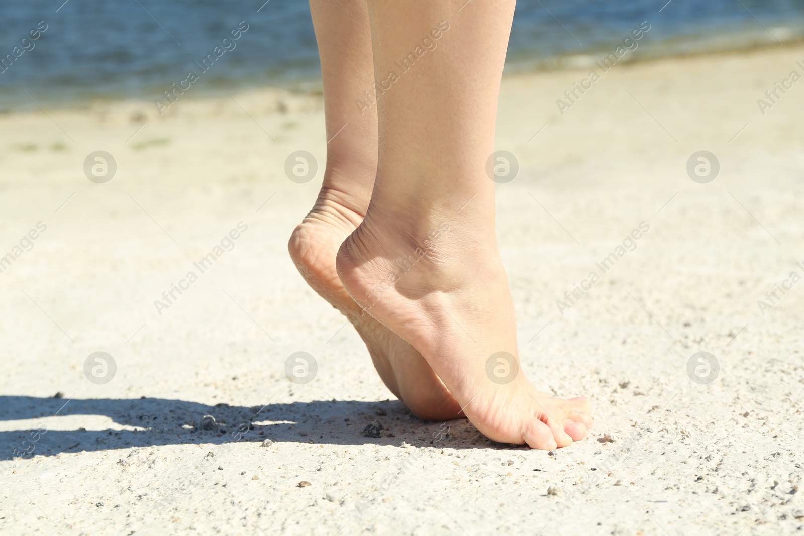 Photo of Woman walking barefoot on sand outdoors, closeup