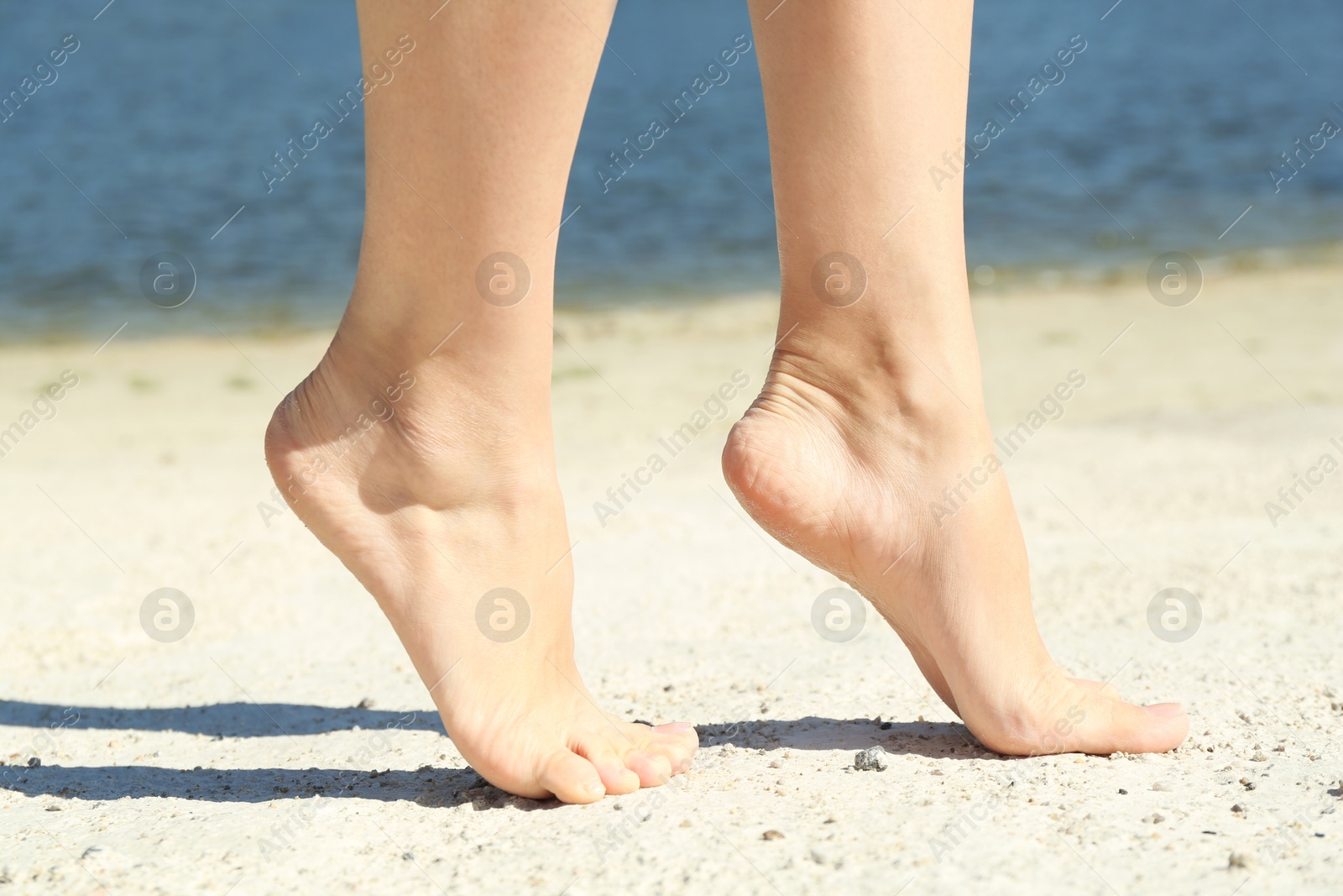 Photo of Woman walking barefoot on sand outdoors, closeup