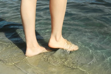 Photo of Woman walking barefoot through water on riverbank, closeup