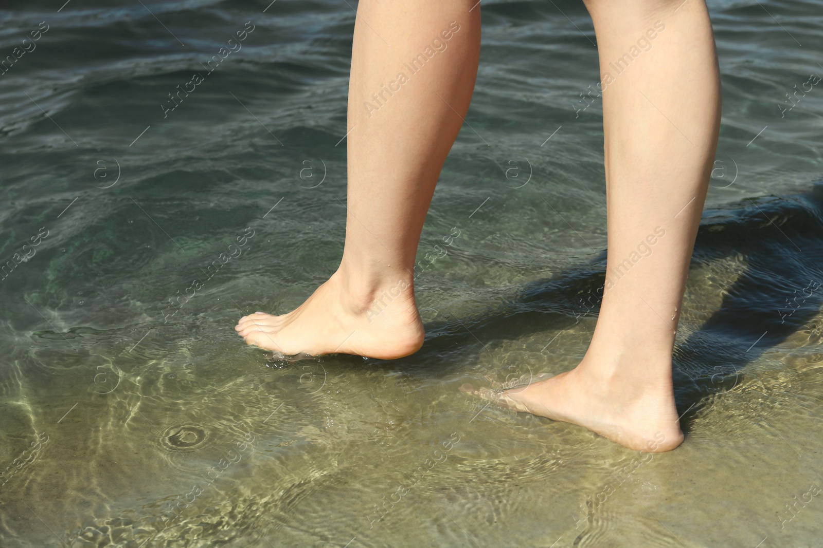 Photo of Woman walking barefoot through water on riverbank, closeup