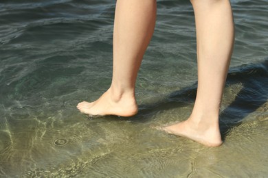 Photo of Woman walking barefoot through water on riverbank, closeup