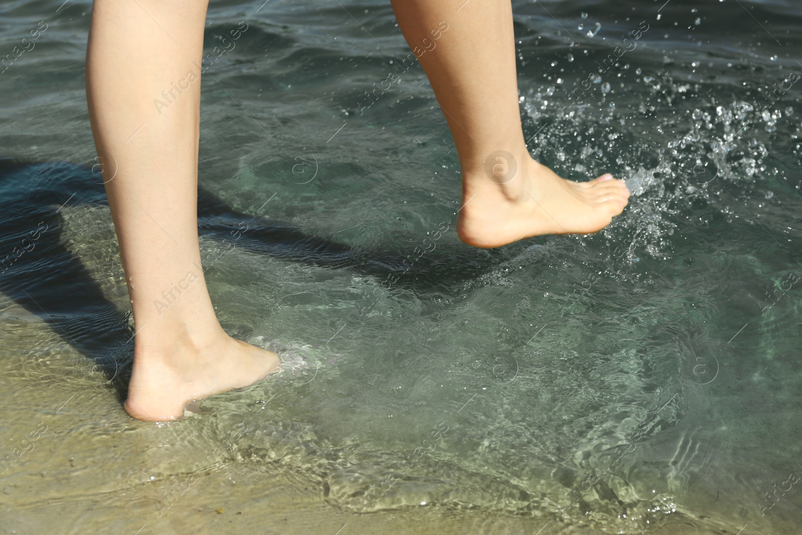 Photo of Woman walking barefoot through water on riverbank, closeup