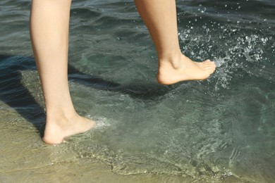 Photo of Woman walking barefoot through water on riverbank, closeup