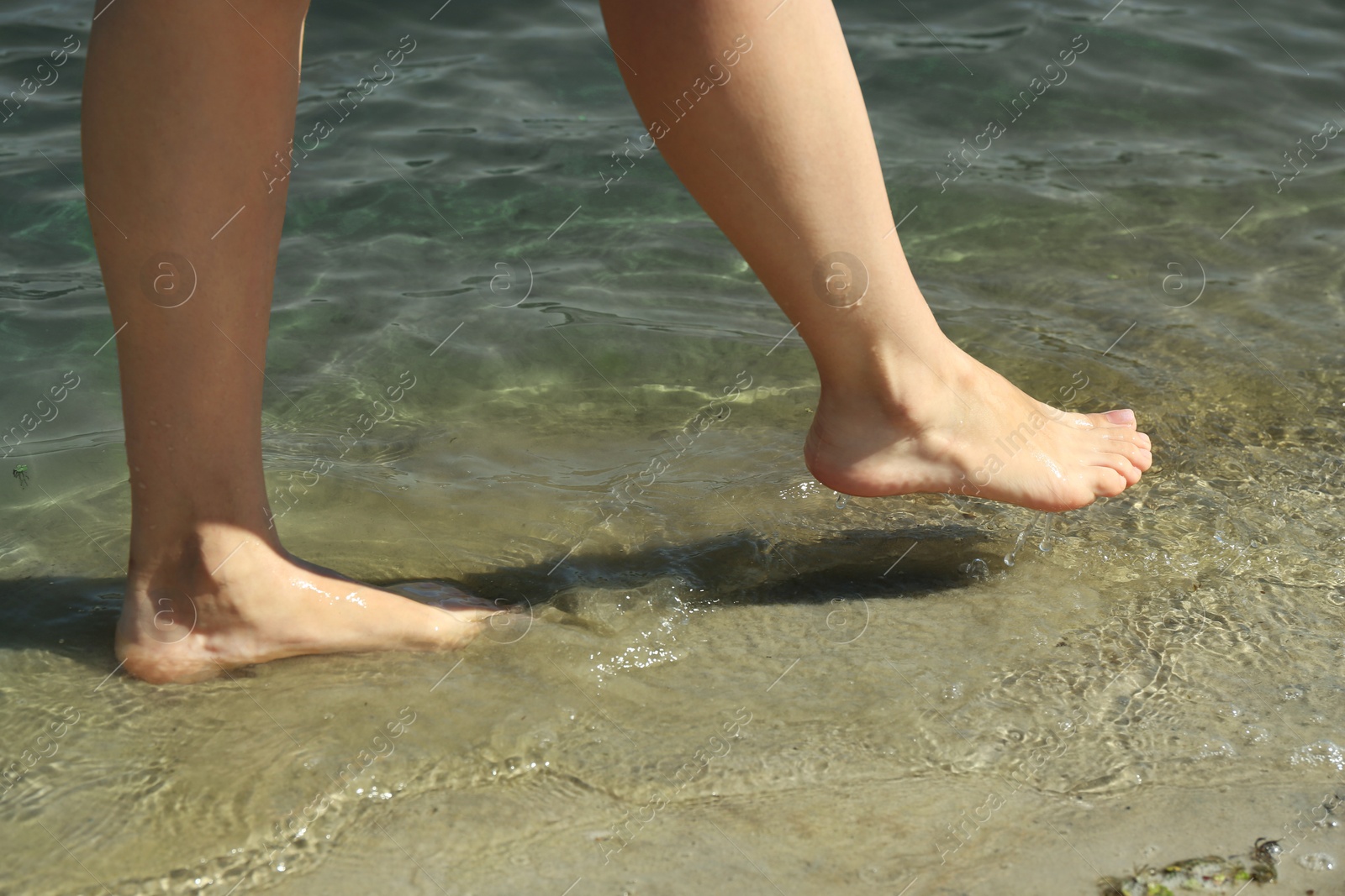 Photo of Woman walking barefoot through water on riverbank, closeup