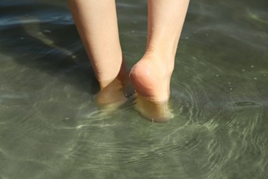 Photo of Woman walking barefoot through water on riverbank, closeup