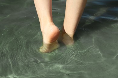 Photo of Woman walking barefoot through water on riverbank, closeup