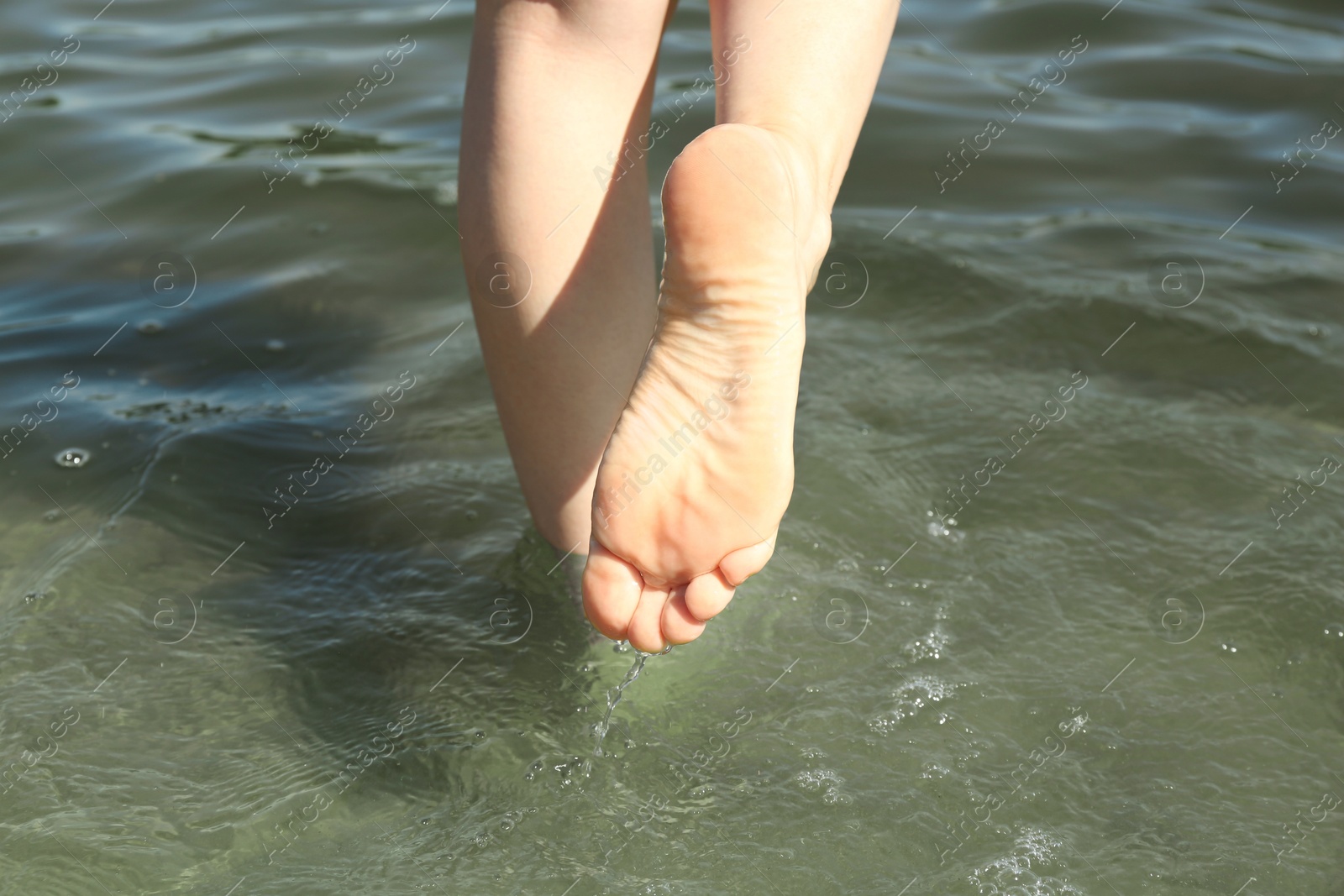 Photo of Woman walking barefoot through water on riverbank, closeup