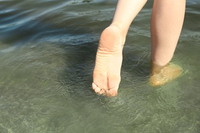 Photo of Woman walking barefoot through water on riverbank, closeup