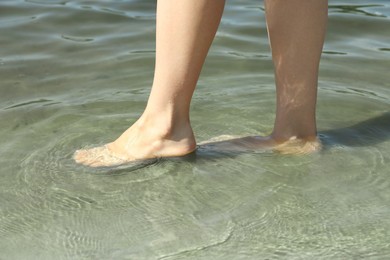 Photo of Woman walking barefoot through water on riverbank, closeup