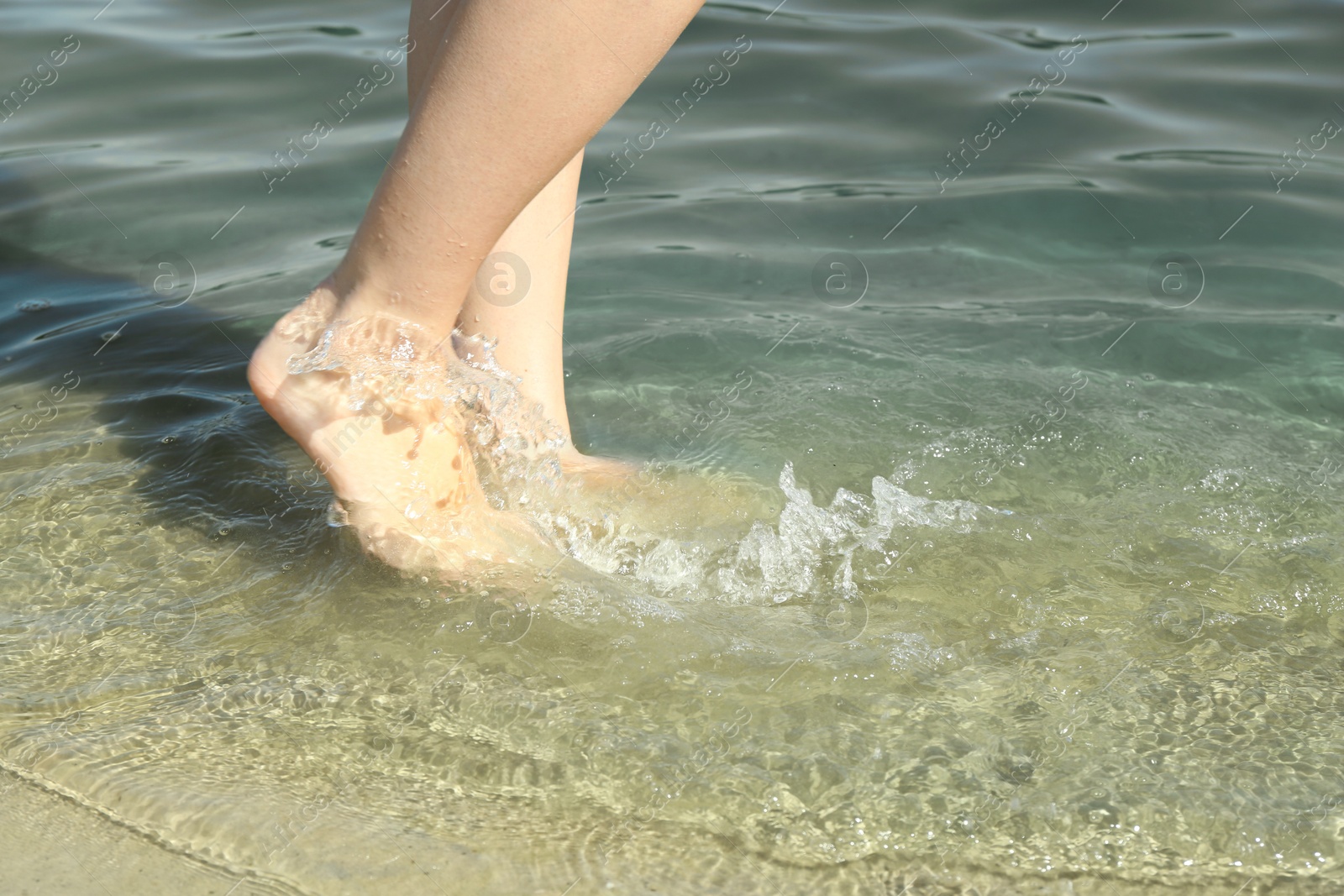 Photo of Woman walking barefoot through water on riverbank, closeup