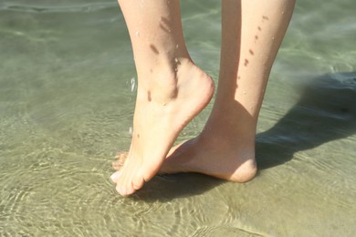 Photo of Woman walking barefoot through water on riverbank, closeup