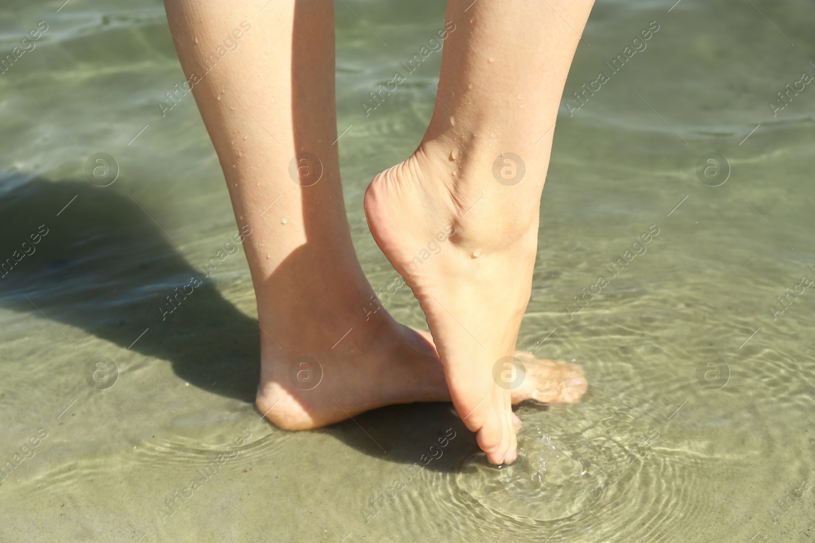 Photo of Woman walking barefoot through water on riverbank, closeup