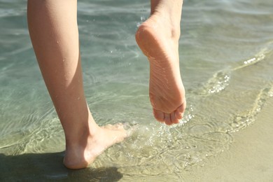 Photo of Woman walking barefoot through water on riverbank, closeup