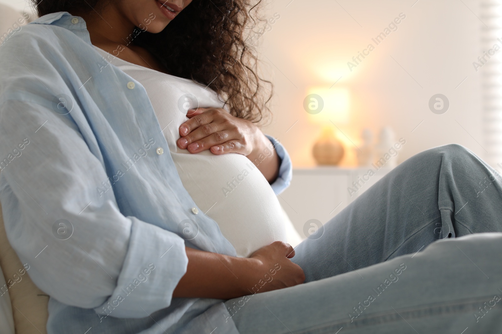 Photo of Pregnant woman touching her belly at home, closeup