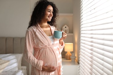 Portrait of beautiful pregnant with cup of drink near window at home