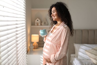 Portrait of beautiful pregnant with cup of drink near window at home