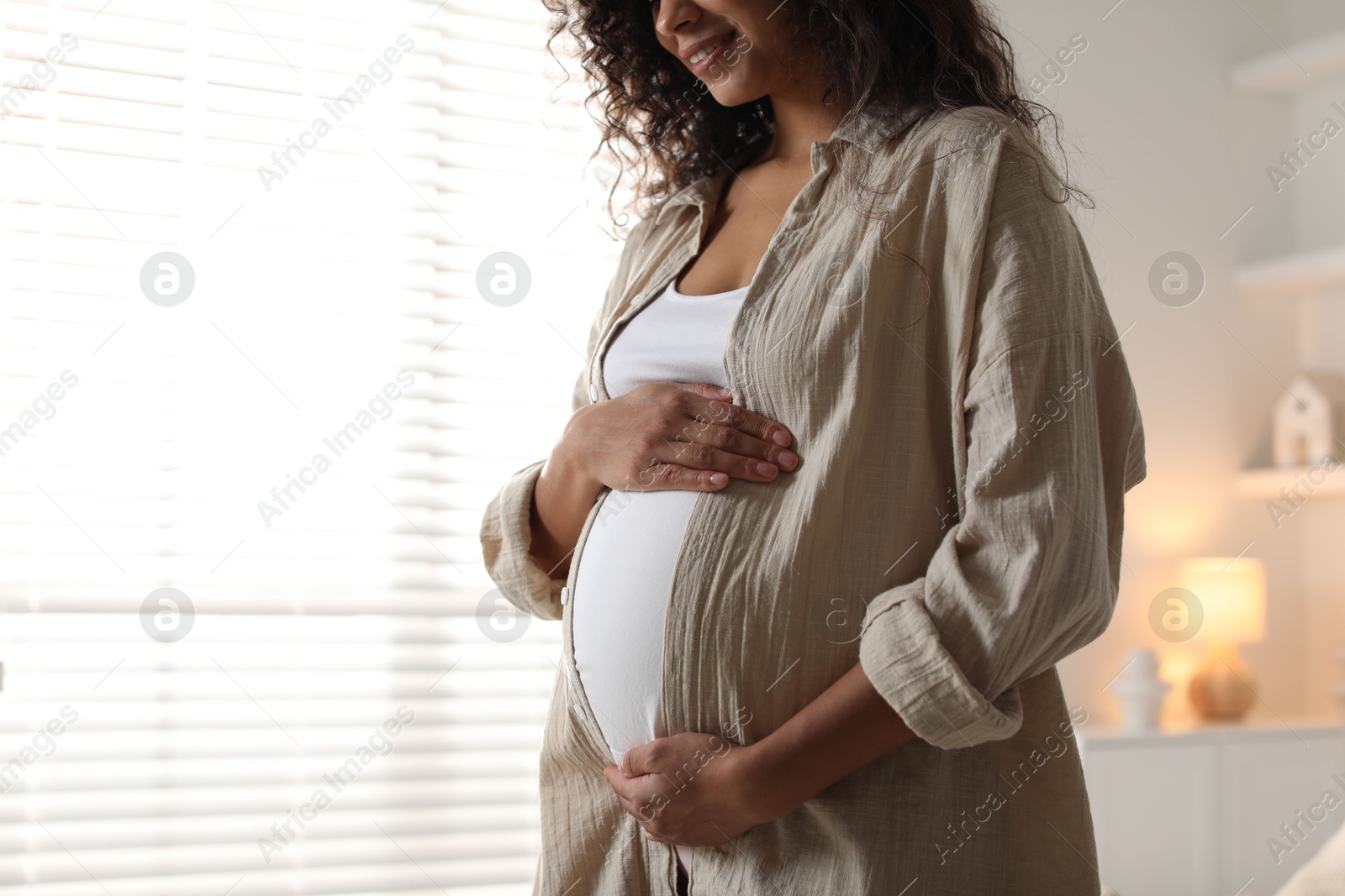 Photo of Pregnant woman near window at home, closeup