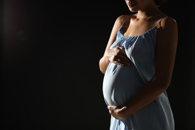 Photo of Pregnant woman on black background, closeup. Space for text