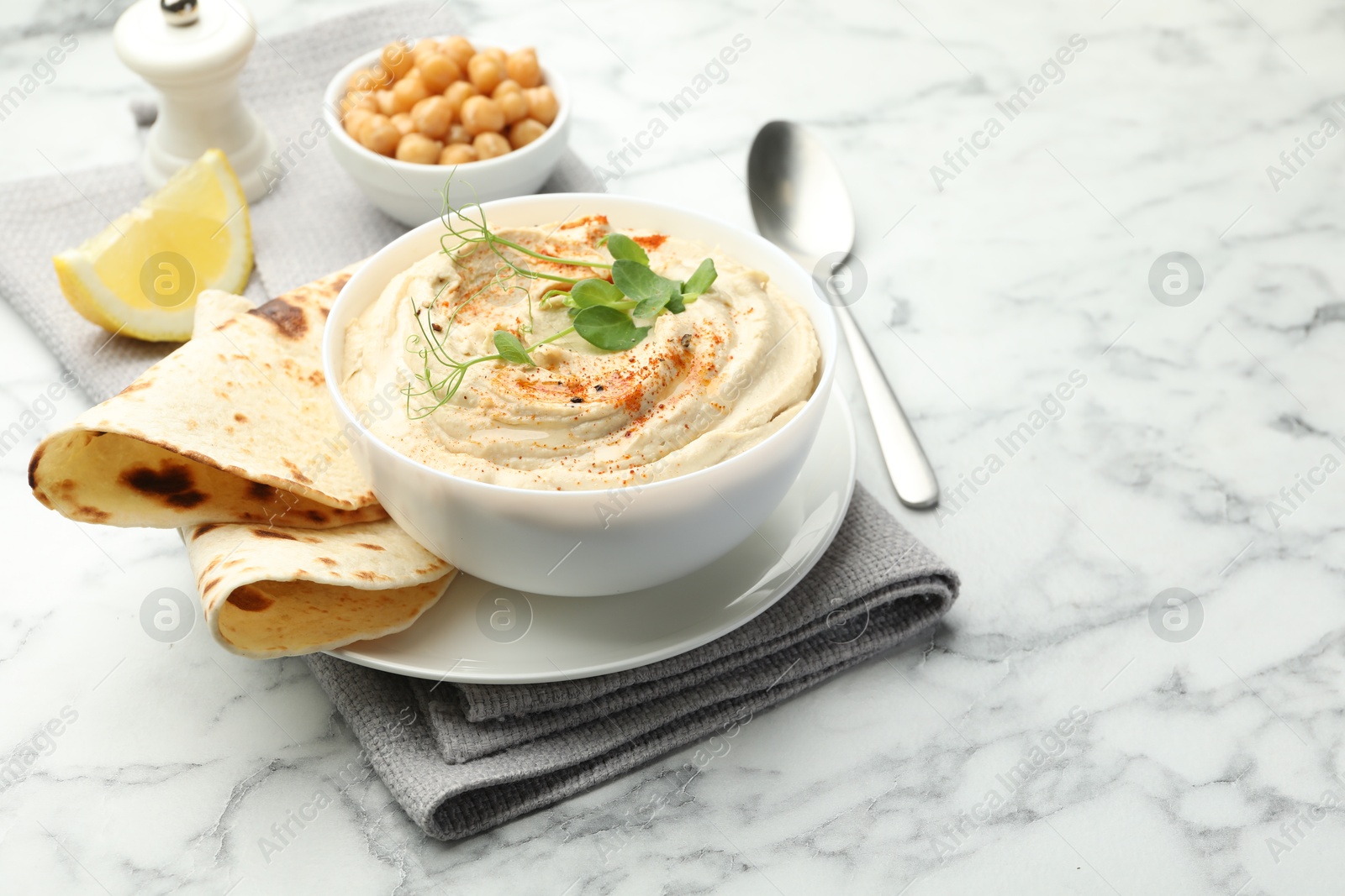 Photo of Delicious hummus with paprika, pita and chickpeas on white marble table