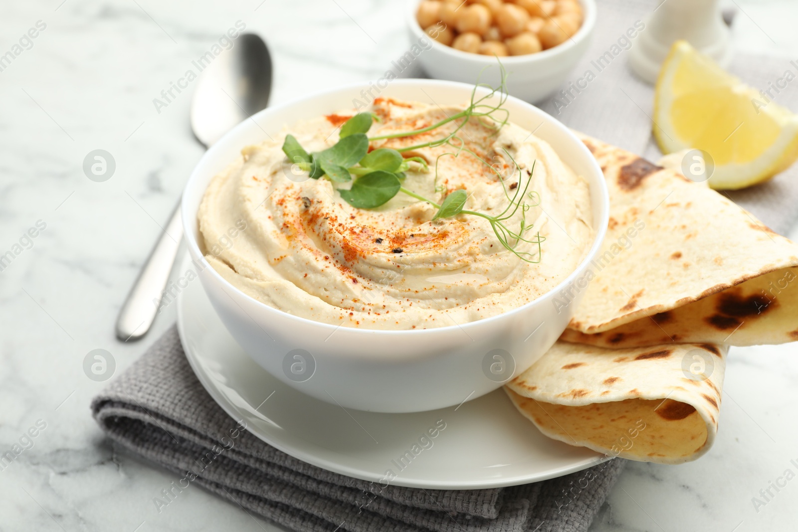 Photo of Delicious hummus with paprika, pita and chickpeas on white marble table, closeup