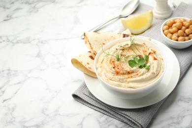 Delicious hummus with paprika, pita and chickpeas on white marble table, space for text