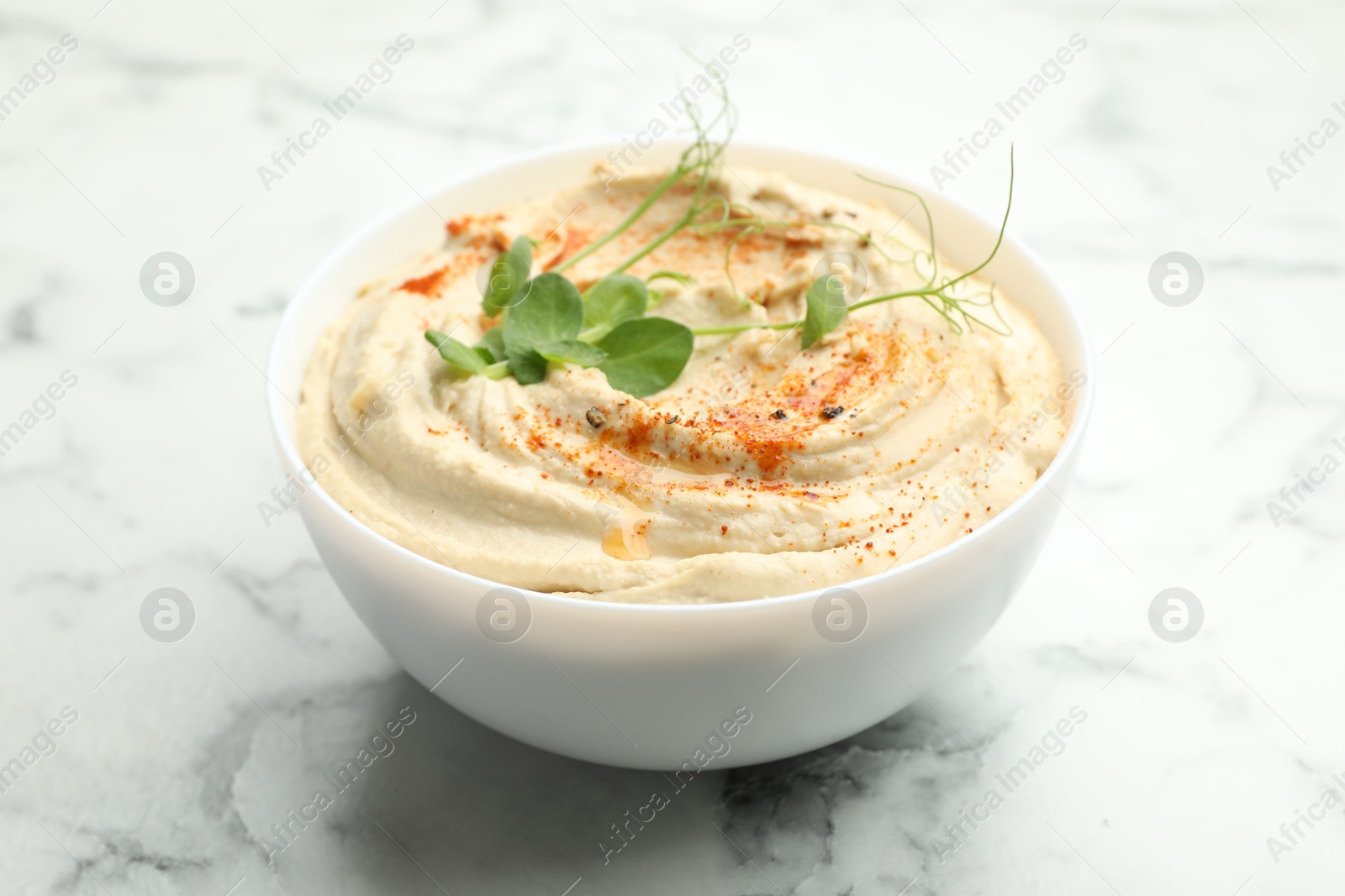 Photo of Delicious hummus with paprika in bowl on white marble table, closeup